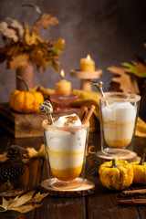 Two glasses of an orange pumpkin spice latte coffee drink with whipped cream, brass drinking straw and cinnamon sprinkles