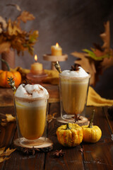 Two glasses of an orange pumpkin spice latte coffee drink with whipped cream, brass drinking straw...