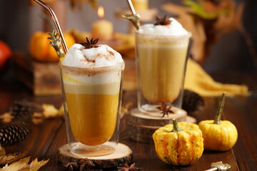 Two glasses of an orange pumpkin spice latte coffee drink with whipped cream, brass drinking straw...