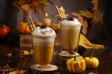 Two glasses of an orange pumpkin spice latte coffee drink with whipped cream, brass drinking straw...