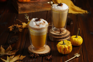 Two glasses of an orange pumpkin spice latte coffee drink with whipped cream, brass drinking straw and cinnamon sprinkles