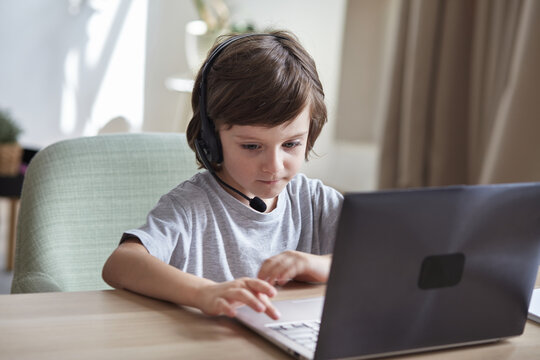 Serious focused boy preschooler learning online through video chat on a laptop. Child studying computer work, typing, and coding. A kid gamer is streaming and playing a video game.