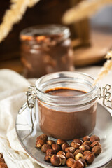 Homemade hazelnut cocoa chocolate cream in mason jar on plate surrounded by hazelnuts
