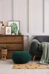 Stylish living room interior with knitted pouf, sofa and wooden chest of drawers