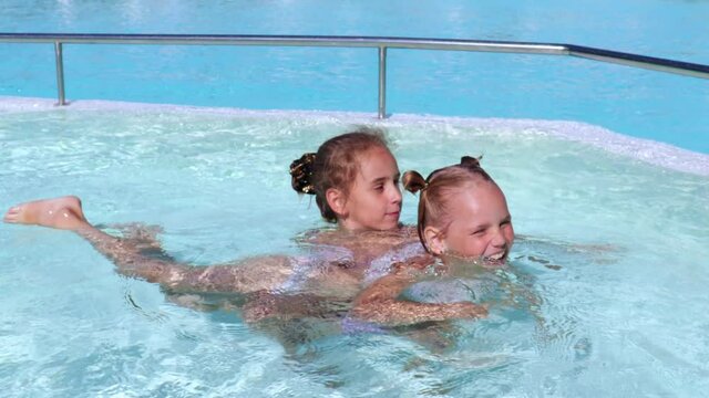 two European girls sisters with blond hair and blue eyes, learn to swim in the pool, children play in the water. Summer travel family hotel vacation tourists great mood