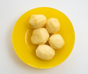Five fresh peeled potatoes in the yellow plate on white background