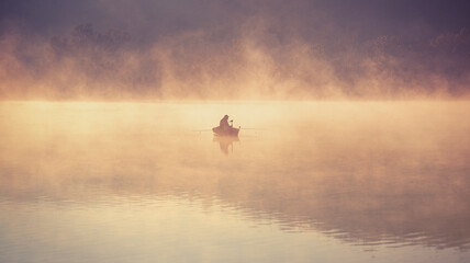 Early morning fishing on a steaming lake in October, in the golden light. - 464266762