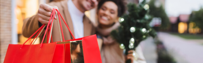 blurred interracial couple with christmas shopping bags, banner.