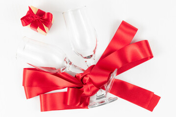 two champagne glasses, a gift box and a red silk ribbon on a white wooden table. close-up