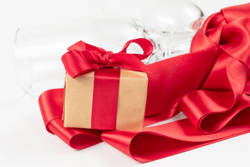 two champagne glasses, a gift box and a red silk ribbon on a white wooden table. close-up