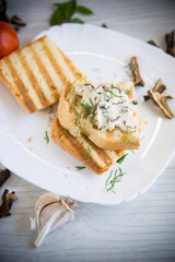 fried bread toast with cheese spread with boiled dried mushrooms on a wooden table.