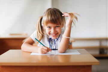 Naklejka premium Happy cute little girl child at school desk, learning concept, private small school, extracurricular activities
