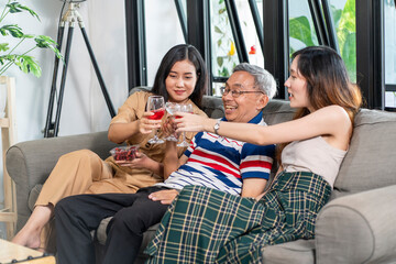 Granddaughter, daughter and grandfather of three generations sitting on the sofa watching TV and celebrating drinks together, having a happy family in the house. 