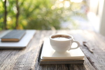 Coffee in ceramic white cup and notebook under sunlight