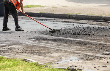 Worker laying new asphalt on city street, closeup. Road repair service