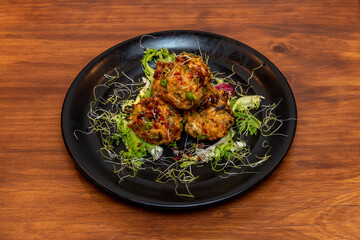 Asian recipe of spiced pork balls in tempura batter with lettuce and bean sprouts on black plate