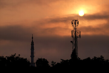 mosque minaret and communication tower during sunrise. radio frequency transmission tower