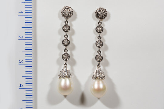 Long designer Gold earring with pearls and diamonds on a white background next to the ruler