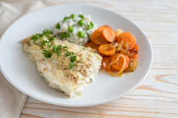 Cod fillet with parsley garnish, carrots and green pea rice on a white plate, healthy fish meal, selected focus