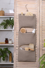 Storage with essentials hanging on wooden folding screen in bathroom. Stylish accessory