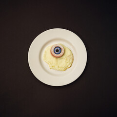 Minimalist concept made with sunny side up egg with blue eye instead of yolk on black background. Spooky halloween concept.