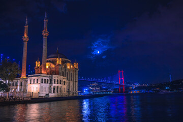 Fototapeta na wymiar Ortaköy Mosque and Bosphorus Bridge during blue hour, full moon and blue night Sky. One of the most popular locations on the Bosphorus, Istanbul, Turkey.