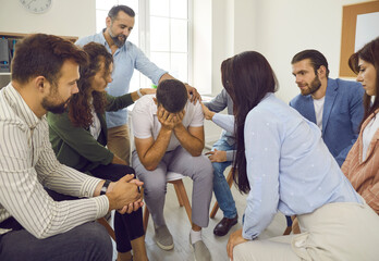 Young businessman in trouble shared his problem with colleagues who comfort him. Employees express...