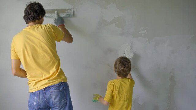 A young man and his son are doing a walls renovation in their home. They are applying putty to the wall. Make renovation yourself. Teaching children how to do repairs by your own