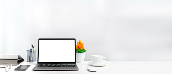 A laptop is a blank white screen on a table in an office. Concept Working using technology smartphones, notebook, coffee cup. Copy space on right for design or text, Closeup, Gray, and blur background