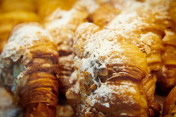 Almond croissants in a pastry shop window. Dessert covered with powdered sugar and almond slices.