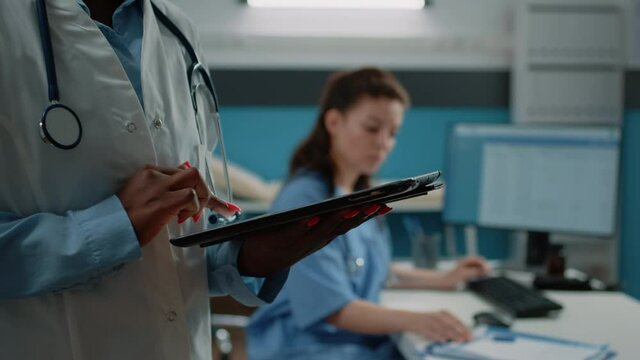 Close up of african american doctor using tablet with touch screen for healthcare information in cabinet. Black medic with white coat and stethoscope holding modern gadget for medical care