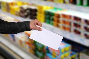 male hand holding a blank sheet on a blurred background, a row of shelves with groceries in a...