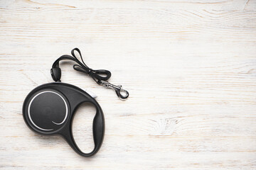 Black retractable leash for dogs on a wood background, space for text. Flat lay.