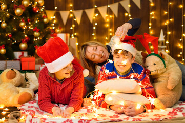 Family posing in new year or christmas decoration. Children and parents. Holiday lights and gifts. Wooden background with illumination. Christmas tree decorated with toys.