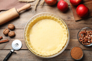 Flat lay composition with raw dough and ingredients for apple pie on wooden table