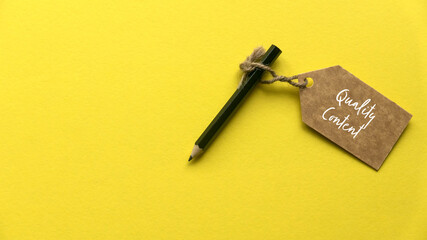 A pencil and brown tag written with quality content on yellow background.