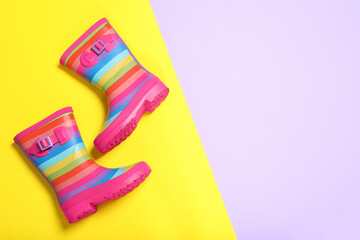 Pair of striped rubber boots on color background, top view. Space for text