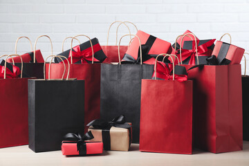 Paper shopping bags and gift boxes on table near white brick wall. Black Friday sale