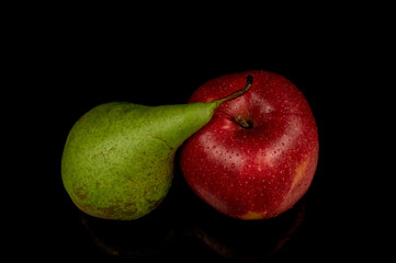Red apple and green pear on a black background. Water droplets on fresh fruit