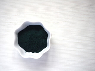 Spirulina powder in a small white bowl on a white background. Close up, top view, copy space.