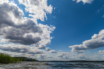 Obraz premium Summer landscape with river, opposite bank and grass and sky with clouds