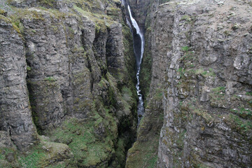 wąski wodospad glymur w islandii spływający po omszonych skałach