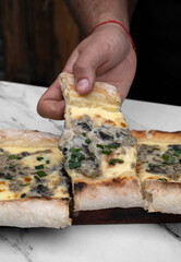 Gastronomy. Italian food. Male caucasian hand holding a slice of pizza with mozzarella cheese, mushrooms and green onions in the restaurant marble table.