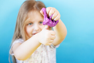 Obraz na płótnie Canvas Blonde girl hold purple slime isolated on a blue background. child playing with a slime toy. Making slime. Copy space.