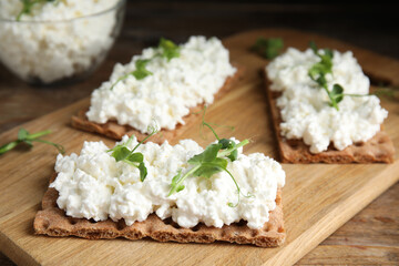 Crispy crackers with cottage cheese and microgreens on wooden table, closeup