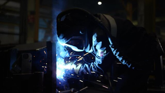 A welder in a helmet is working at the plant