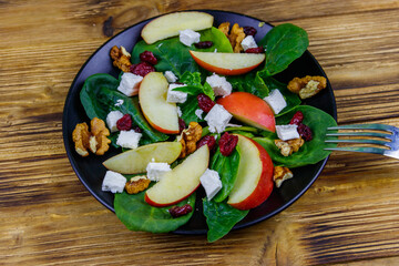 Autumn spinach salad with apple, feta cheese, walnut and dried cranberry on wooden table. Healthy vegetarian food