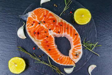 Raw salmon steak with spices on black slate. Top view