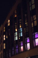 colorful lights in windows in a building block of flats apartments - obrazy, fototapety, plakaty