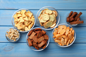 Different crispy rusks in bowls on light blue wooden table, flat lay
